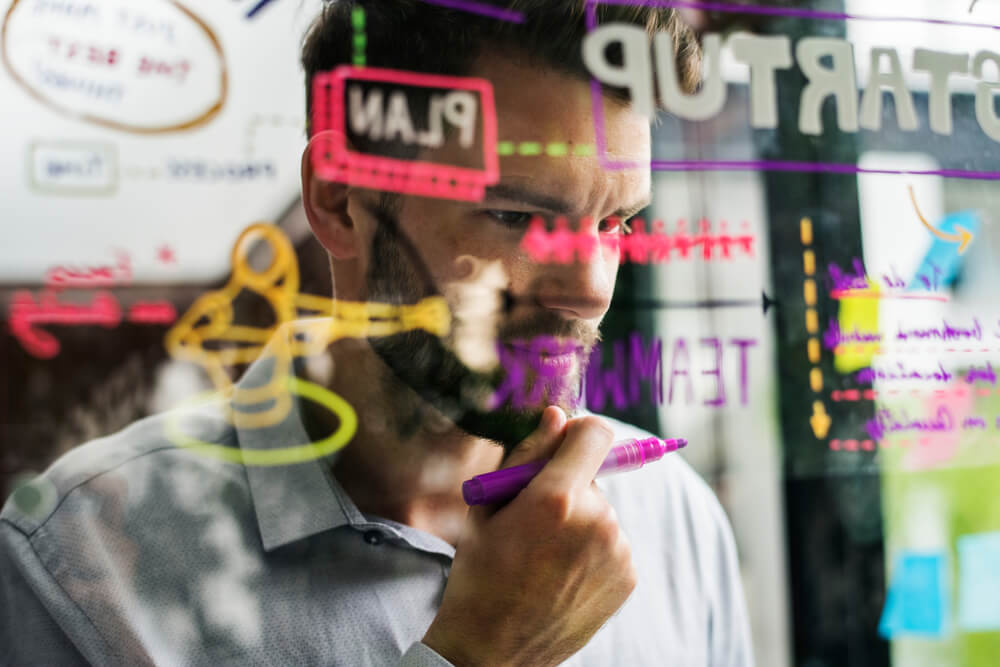 homem concentrado segurando caneta a frente de anotações coloridas em vidro